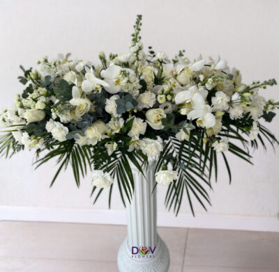 Aranjament funerar alb pe suport înalt, cu orhidee, trandafiri și frunze decorative